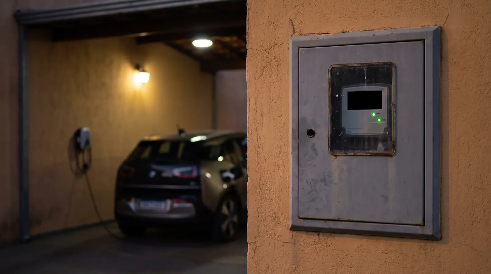 Medidor de energia na parede de uma casa, com um carro elétrico carregando ao fundo