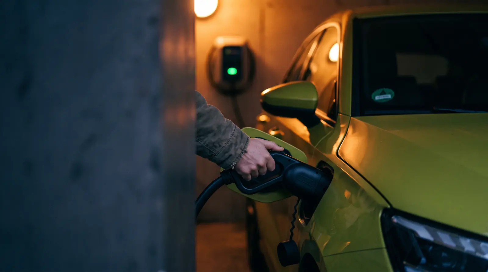 Mão encaixando o conector de recarga na entrada de um carro elétrico